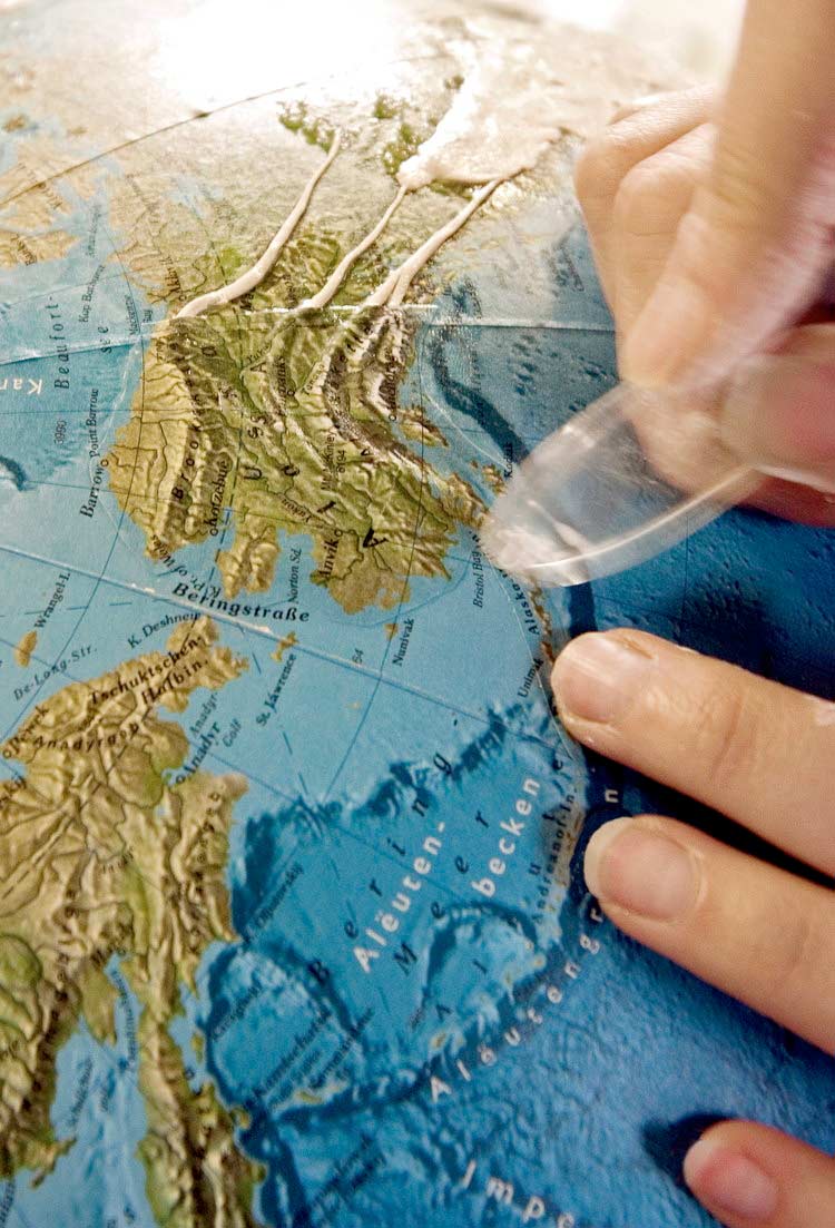 Hand mit transparentem Werkzeug auf Reliefkarte, Fokus auf Insel und umliegendes Meer.